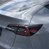Close-up of the rear of a silver Tesla Model Y with Volcano Gray Glossy SelfRepair Nano-Coated PPF, highlighting the taillight and curves as sky and clouds reflect beautifully on the ochranný film na lak surface.