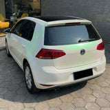 A white Volkswagen hatchback, protected by White Diamond Pine Green Glossy SelfRepair Nano-Coated PPF, is parked on a hexagonal stone driveway in front of a modern building with glass windows and yellow chairs inside.